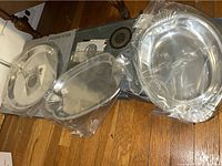Three Wilton Armetale metal serving platters with scalloped edges wrapped in plastic, laid on wooden floor near cardboard boxes.