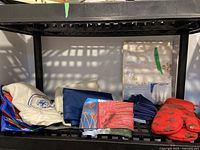 Wide view of assorted kitchen linens including tablecloths, napkins, aprons, and oven mitts arranged on shelving unit