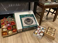 Lot arranged on floor showing boxed cast iron tree stand and three boxes of assorted Christmas balls and ornaments, vintage style colors and finishes