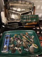 Full lot shown with metal serving tray, green tray holding assorted silver spoons, and carving set in case