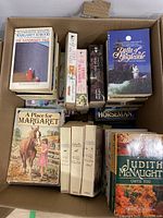 Top view of a box with multiple softcover books including The Handmaid's Tale by Margaret Atwood, A Place for Margaret by Debbie Macomber, Tilly Trotter series by Catherine Cookson, Judith McNaught, and other fiction titles.