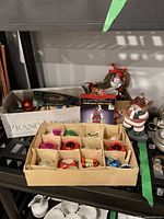 Close-up of the cardboard sectioned box showing colorful vintage glass teardrop and bell-shaped ornaments in pink, silver, orange, red, green, blue, and white