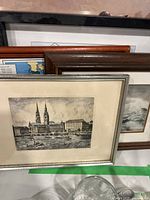 Close-up of several framed prints stacked showing historic cityscapes and framed map edges.