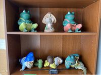 Wooden shelves holding figurines: two frogs, one mouse on upper shelf; gnomes, a caterpillar, and a frog on lower shelf, all vintage handpainted collectibles
