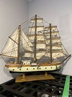 Full view of the wooden ship model on its stand showing cream hull and multiple fabric sails with rigging.
