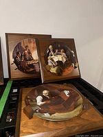 Three Norman Rockwell ceramic plates depicting family scenes, each framed in wooden mounts, displayed grouped on a surface.