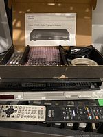 Photo of Panasonic DVD player and Cisco DTA50 Digital Transport Adapter with accessories inside original box, bubble wrap, and two remote controls in front.