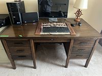 Front view of vintage wooden desk showing 7 drawers with metal handles, desktop with computer monitor, keyboard and mouse.