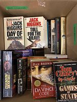 Box packed with books by Jack Higgins, Dan Brown, John Grisham, Tom Clancy, Dean Koontz, Khaled Hosseini and others. Mixture of hardcover and paperback including 'The Da Vinci Code' and 'Games of State'.