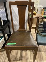 Front view of traditional brown wooden dining chair with leather seat showing wear.