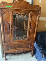 Full china cabinet front view showing carved wood and decorative metal scrollwork glass door, single drawer below