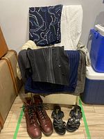 Women's clothing draped over chair with two pairs of women's footwear placed beneath. Shoes include oxblood lace-up shoes and black heeled sandals.