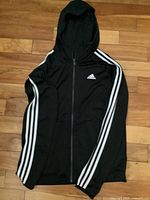 Front view of black Adidas track top hoodie with full zipper, hood, and white three stripes on sleeves.