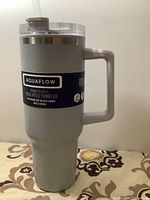 Grey Aquaflow insulated tumbler with handle and clear lid, side view showing label and handle