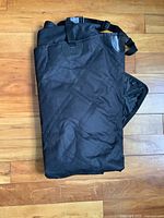 Photo of a folded black barbecue grill cover made of heavy-duty fabric with adjustable straps.