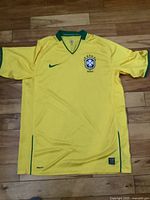 Front view of yellow Brazil soccer jersey laid flat on hardwood floor, showing full shirt with green accents.