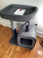 Full view of gray Catry Eclipse cat tower with cushioned top perch, hideout base, and scratching posts, placed on wooden floor.