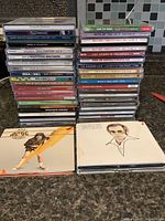 Photo of stacked music CDs showing various artists and album titles, focusing on the front and spine of the jewel cases.