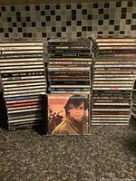 Photo showing large stacked lot of music CDs with various artists and titles visible on spine labels.