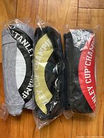 Three new Coors Light Stanley Cup champion T-shirts, packed in original sealed plastic bags, showing front logo designs in different colors.