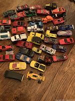 Top-down view of approximately 40 older diecast cars scattered on a wooden surface, showing a variety of models and colors including red, yellow, blue, and orange vehicles.