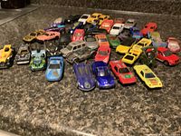Wide view of approximately 40 diecast toy cars grouped on a surface, showing range of colors and styles from sports, rally, classic to off-road models