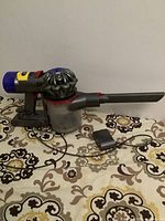 Full view of Dyson handheld vacuum cleaner with charger placed on patterned surface.