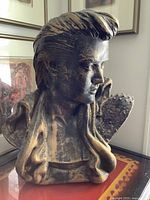 Front and side views of the dark-finished bust sculpture styled as Elvis Presley with a headless top and detailed textured clothing.