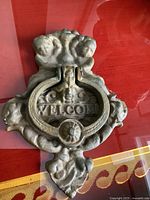 Photo showing front view of heavy metal door knocker with intricate design and 'WELCOME' text.