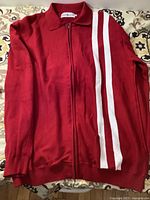 Red zippered jacket laid flat showing the full front and white stripes detail on left side.