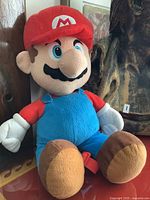 Full view of the Super Mario plush toy sitting upright showing outfit and overall shape.