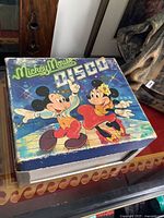 Front view of the portable turntable with colorful Mickey Mouse and Minnie Mouse disco-themed artwork on the lid.