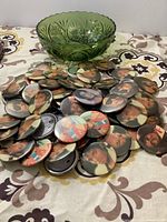 Green pressed glass bowl sitting on floral patterned cloth next to a pile of Michael Jackson image buttons scattered on surface.