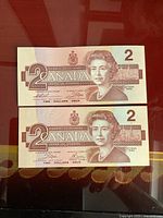 Front side of two Canadian $2 bills featuring Queen Elizabeth II, crisp uncirculated condition.