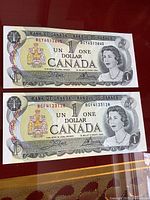 Front view of two Canadian 1 dollar bills showing Queen Elizabeth II and the Canadian coat of arms.