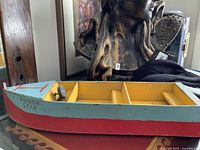 Side view of the old wooden boat-shaped shelf painted blue and yellow with red wave pattern.