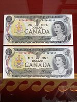Front side of two Canadian one dollar bills showing Queen Elizabeth II portrait and serial numbers.