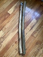 Two wooden rain sticks side by side on wooden floor, showing full length and surface features.