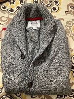 Folded knit sweater showing marled black and white yarn with shawl collar and button details.