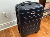 Closed black hard shell Samsonite carry-on suitcase showing textured surface and top handle.