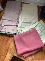 Four vintage wool blankets folded on the floor, varying colors including pink, off-white with stripes, and beige.