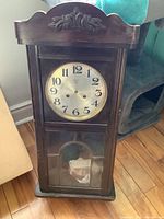 Front view of the vintage wooden chiming wall clock with carved floral decoration and glass door.
