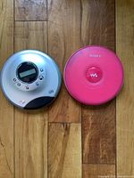 Two portable CD players side by side on wooden floor, showing top views.