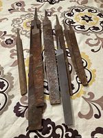 Photo showing seven vintage metal files laid out on patterned fabric background. Includes files with wooden handles and all-metal handles, showing rust and wear.