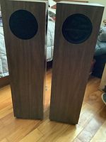 Pair of vintage Epicure M75 micro tower speakers standing on wooden floor showing their wood veneer finish and front black speaker covers.