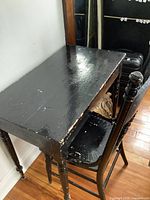 Side view of vintage wooden desk in black paint with worn finish and drawer space under the tabletop, showing chipped and scuffed paint.
