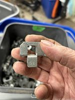 Close-up photo of a silver metal plywood clip held between fingers, stamped with '1/2' and shaped to hold plywood.