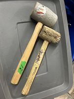 Two rubber mallets placed on a grey plastic surface showing the heads and wooden handles clearly.