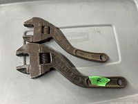 Two vintage adjustable wrenches on a flat light-colored surface, showing rust and wear, marked '12 INCH' on one wrench handle