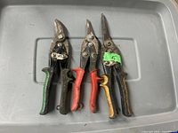 Three pairs of tin snips with different colored handles laid on a gray surface